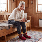 Kvinna i röda Nordic Knit Slipper Socks med kaffe på träsoffan i stugan