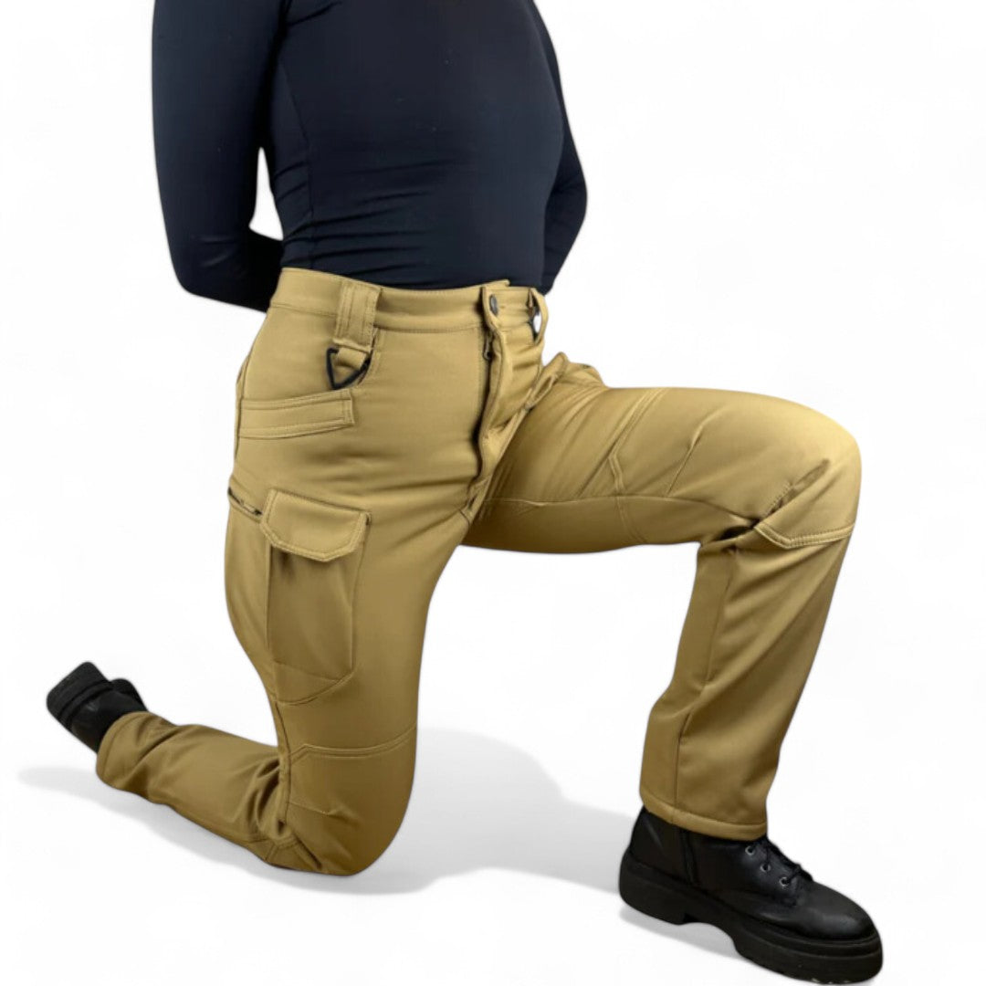 OUTDOORS NORDIC utility fleece pants in tan, featuring multiple cargo pockets, windproof stretch fabric, and a kneeling pose.