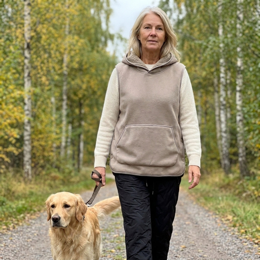 Kvinna runt 60 på hundpromenad i höstig björkskog i beige Sherpa Hoodie Vest och svarta Warm Fleece Pants