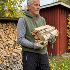 Man bär ved vid ett rött förråd i grön Sherpa Hoodie Vest och svarta Warm Fleece Pants