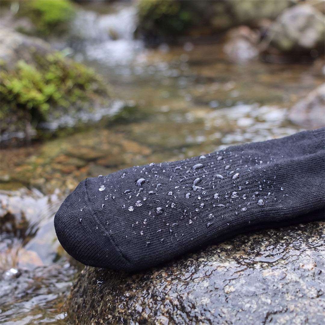 Närbild på vattendroppar som pärlar sig på Waterproof Hiking Socks i svart vid en bäck
