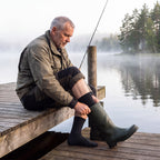 Man i svarta Waterproof Hiking Socks drar på sig gummistövlar på bryggan vid sjön
