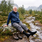 Man i svarta Waterproof Hiking Socks vilar på en sten vid en blöt fjällstig